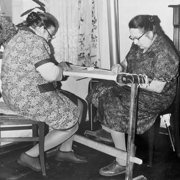 Zwei Frauen sitzen in Heimarbeit am Näh-(Stick-)Rahmen